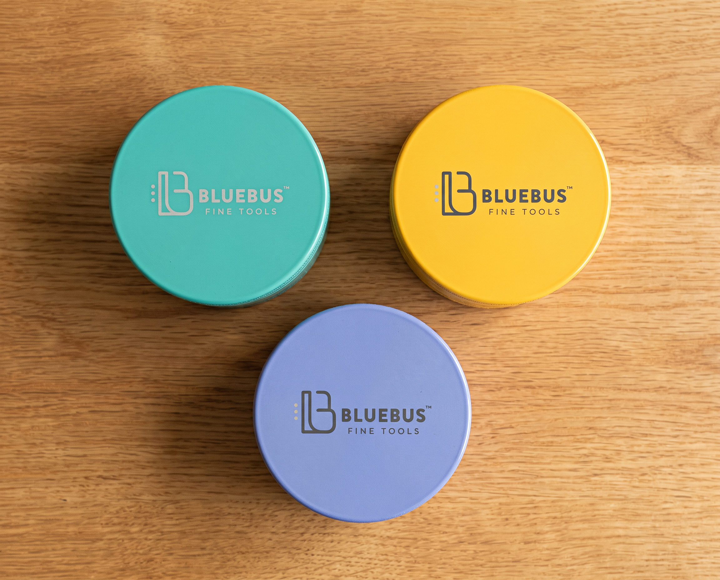 Three GC ceramic herb grinders in teal, yellow and lavender arranged on an oak table